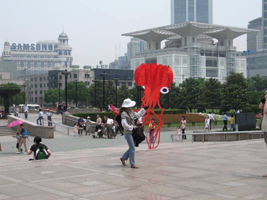 A street vendor holding a bright red kite